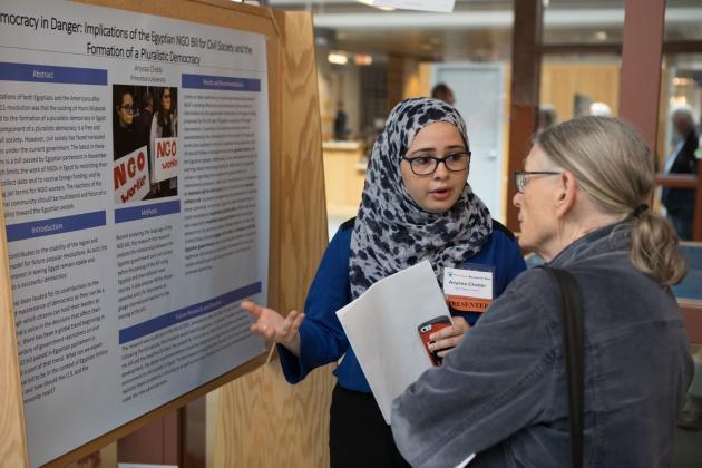 Student standing in front of research poster talking to an audience member